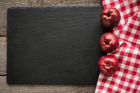 Ripe red apples on wooden board with red checkered napkin around and copy space on black slate dish.の写真素材