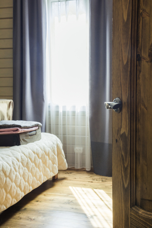 Opened wooden door and view to the bedroom. Open suitcase with clothes on the bed.の写真素材