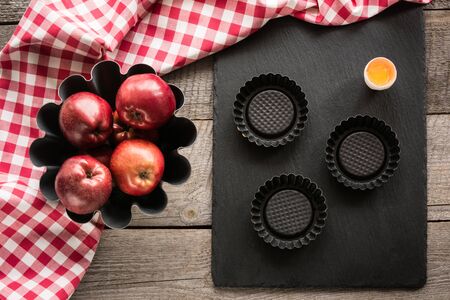 Ripe red apples on wooden board with red checkered towel around and accessories for baking. Copy...