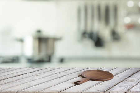 Blurred and abstract kitchen background. Empty wooden tabletop with cutting board  and defocused modern kitchen for display or montage your products.の写真素材