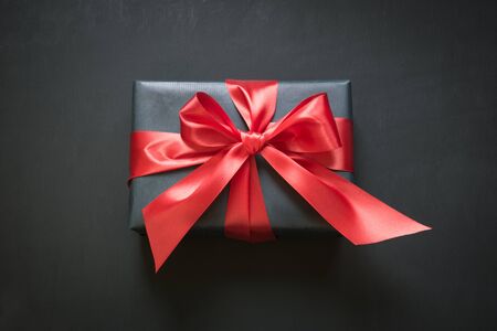 Gift box wrapped in black paper with red ribbon on black surface. Top view.の写真素材