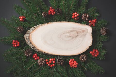 Christmas composition made of christmas tree branches, red berries with wooden saws as empty blank on black. Top view and copy space. concept. Matte image.の写真素材