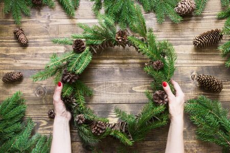 Making Christmas wreath using fresh and all natural materials. Christmas wreath with fir branches on wooden board in female hand. Flat lay. Top view.の写真素材