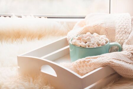 Blue cup of hot chocolate with marshmallow on white windowsill with furskin for rest. Holiday concept. Home style.の写真素材