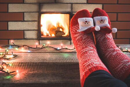 Feet in woollen red socks by the fireplace. Female relaxes by warm fire and warming up her feet in christmas socks. Close up on feet. Tabletop for display your christmas product. Christmas holiday.の写真素材
