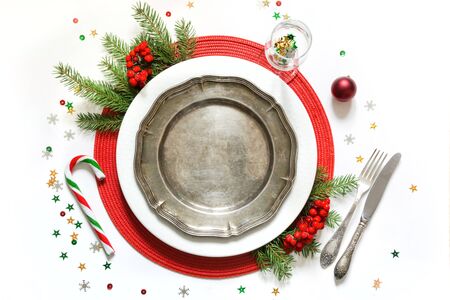 Christmas table setting with vintage dishware, silverware and red decorations on white background....