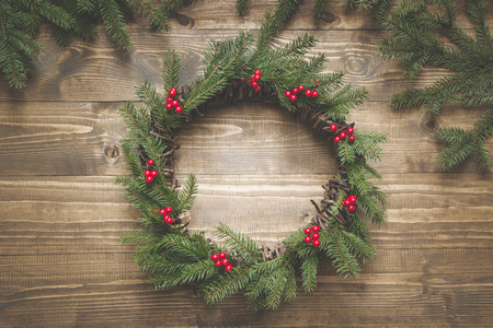 Christmas wreath made of spruce branches with holly berries on wooden board. Flat lay. Top view.