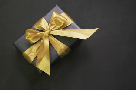 Gift box wrapped in black paper with gold ribbon on black surface. Top view.の写真素材