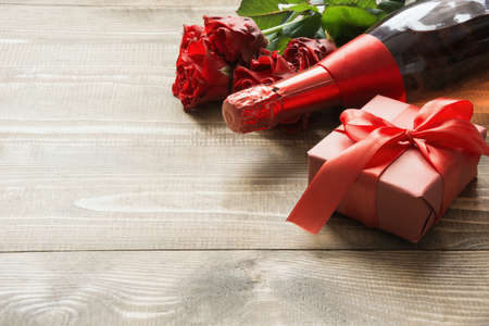 Valentines day greeting card with bouquet red rose flowers, a bottle of champagne and gift box on wooden table. Copy space. Close up.の写真素材