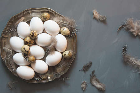 White chicken and quail eggs in vintage plate on gray neutral background. Top view and copy space.の写真素材