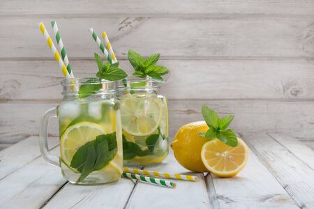 Summer drink, water with lemon, ice and mint in mason jar on a white wooden background.の写真素材