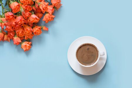 Bouquet of bush orange roses and cup of black coffee on pastel blue background. Flat lay. Copy space. Spring.の写真素材