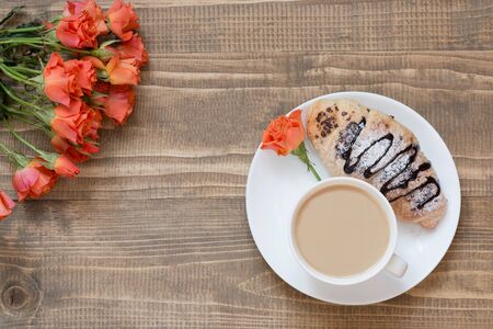 Two delicious freshly baked chocolate croissants and cup of coffee on wooden board. Top view. Female...