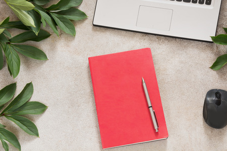Female workplace with laptop, red notebook for notes, pen,  green leaves around on vintage office...