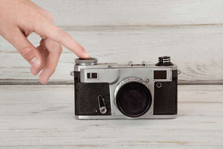 Hand pushing the button of a retro film camera on grey wooden background.