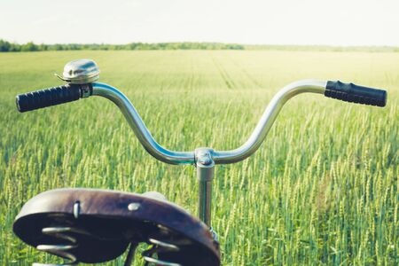 Vintage handlebar with bell on bicycle. Summer day for trip. View of wheat field. Outdoor. Closeup. Detail.の写真素材