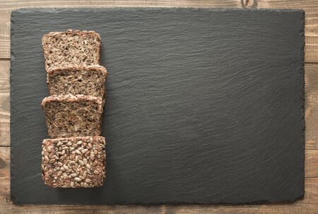 Fitness wholegrain rye bread. Loaf of sliced rye bread with seeds on black slate dish. Top view....