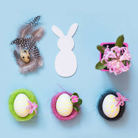 Easter concept. White bunny and painted chicken eggs with pink flower decor on blue. Top view. Flat...