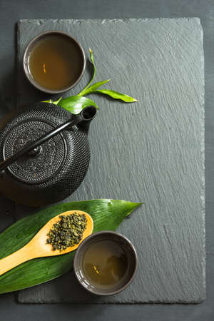Green japanese tea on black slate background. Black teapot and bowl with green tea. Top view with copy space.の写真素材