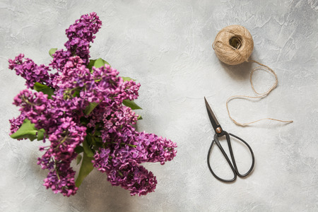 Bouquet of purple lilacs, bonsai scissors and twine on vintage table. Preparation of spring bouquet....