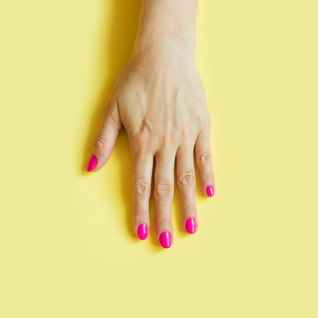 Trendy style of one female hand with pink nail on yellow background. Concept.の写真素材
