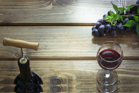 Open bottle of red wine with a glass, corkscrew and ripe grape on a wooden background. Copy space and top view.の写真素材