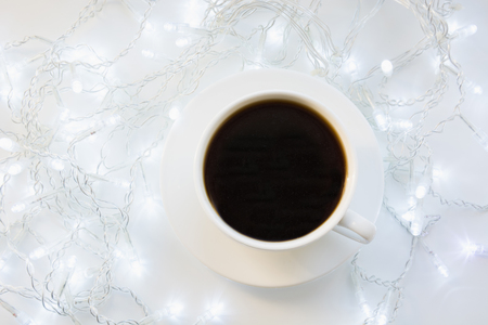 Cup of black coffee on winter white table with garland. Xmas holiday time. Top view.の写真素材