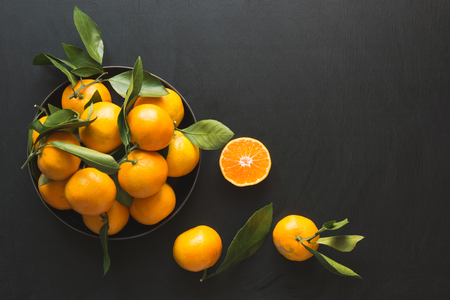Fresh mandarins with leaves in bowl on black. Healthy eating concept. Copy space.の写真素材