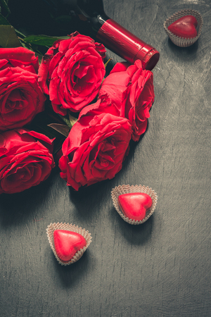 Valentines day greeting card with romantic red roses, wine bottle, heart and red gift box on wooden board.の写真素材