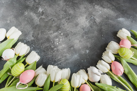 Easter pattern. Border of white tulips, colorful eggs, nest on vintage gray. Top view with copy space.の写真素材