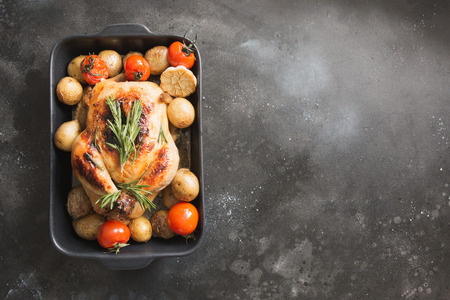 Roasted chicken with potatoes, tomatoes on black table. View from above. Space for text.の写真素材
