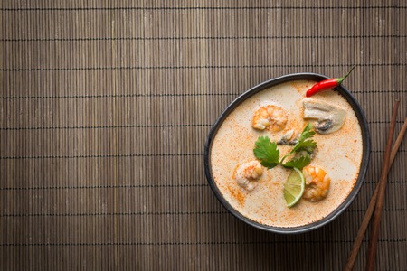 Tom yam kung spicy thai soup with shrimp, seafood, coconut milk, chili pepper on mat. Space for...
