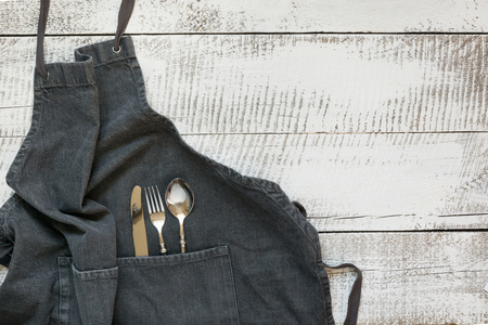 Gray kitchen apron with silverware on wooden table. View from above with space for text. Cooking and kitchen background.の写真素材