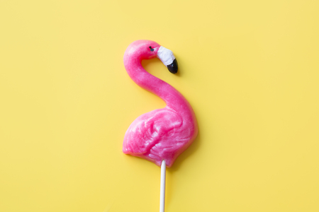 One pink flamingo candy lollipop on yellow background. Top view. Fun tropical jungle vacation. .の写真素材