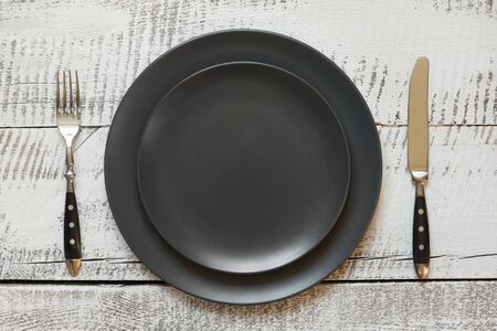 Table place setting with black plate on white wooden table. View vrom above. Horizontal orientation.
