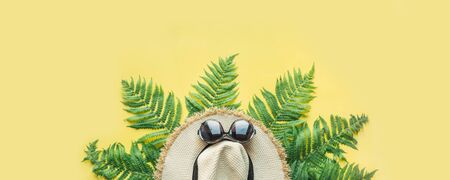Female beach straw hat and fern leaves on punchy yellow. Space for text. Summer travel vacation. View from above. Banner.の写真素材
