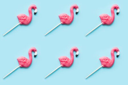 Pink flamingo candy lollipops on pastel blue background. Top view. Food pattern.