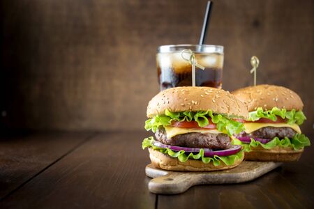 Fresh beef burger with vegetables with cola on dark wooden board. Summer party. Close up. Horizontal orientation. Space for text.の写真素材