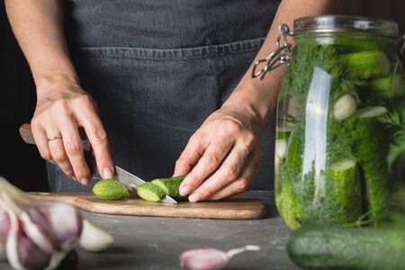 Woman cooking marinated cucumbers with garlic and dill in glass jar. Rustic dark style. Close up.の写真素材