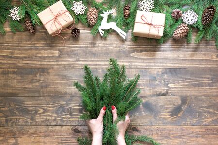 Christmas creative frame composition. Female hand holding spruce branch for making on the wooden background. Top view and copy space.の写真素材