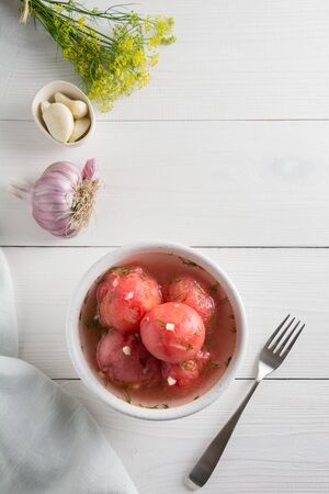 Marinated fermentation peeled tomatoes with garlic and dill, fresh ready to serve on white wooden board. Top view.の写真素材