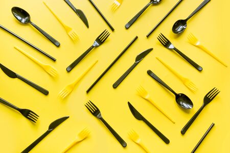 Disposable picnic black knife and forks in diagonal on yellow. Top view. Flat lay. Pattern. Zero waste, save the planet, danger of plastic.の写真素材