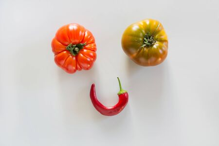 Oddly shaped tomatoes and hot pepper as smiley face on grey. Concept of organic vegetables.の写真素材