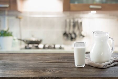 Glass of fresh milk and jug on wooden tabletop with blur kitchen as background. Space for text or display product.の写真素材