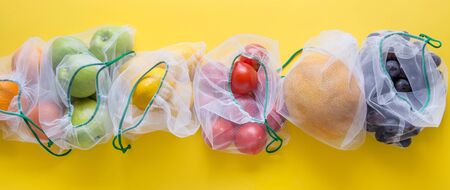 Fruits and summer vegetables in reusable eco friendly mesh bags on bright yellow background. Zero...