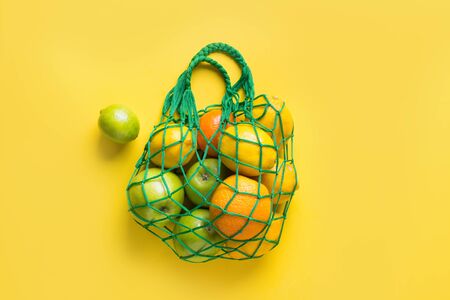 Shopping string bag with friuts, lemon, orange on yellow. Zero waste concept. Space for text. View from above.の写真素材