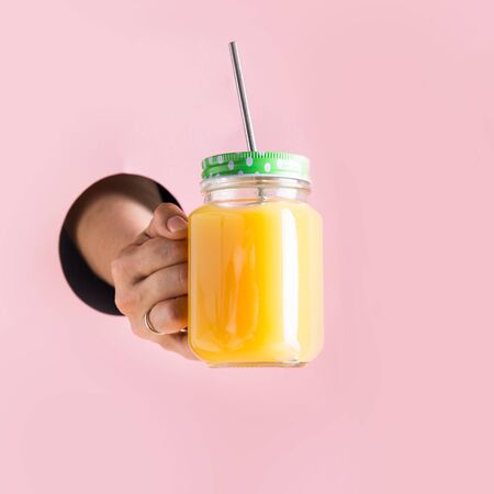 Orange juice in mason jar holding female hand through in hole.の写真素材