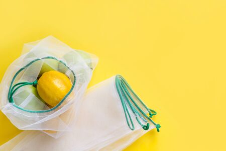Citrics in reusable eco-friendly mesh bags with on yellow background. Zero waste concept. Ecological shopping. Stop pollution. Space for text. View from above.の写真素材