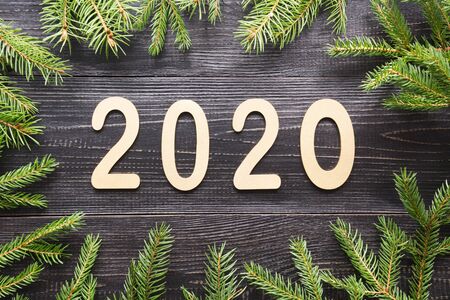 Happy New Year 2020. Golden date, border of evergreen branches on black wooden board. Christmas....