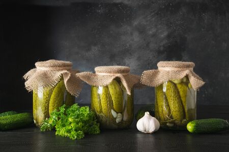 Canned vegetables cucumber in glass jars on wooden dark board. Homemade harvest fall preparations.の写真素材
